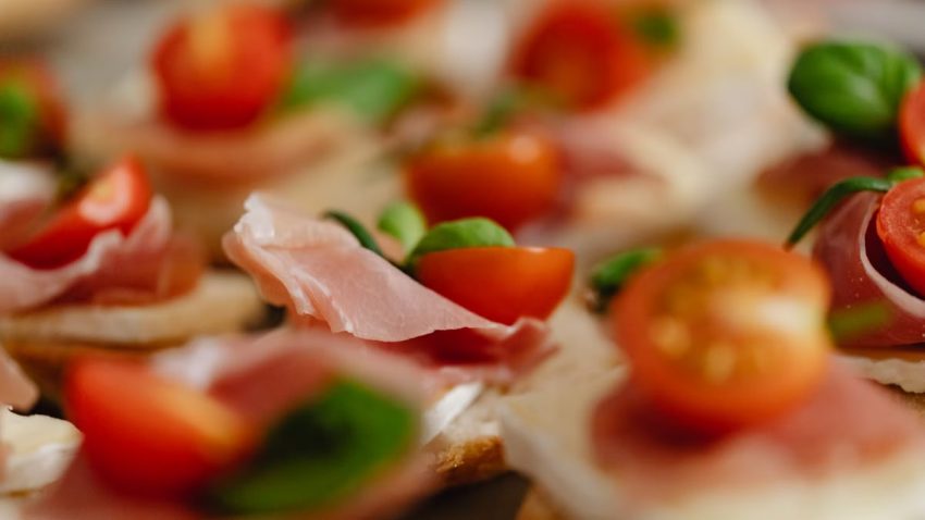 Appetizing canapes topped with prosciutto, cherry tomatoes, and fresh basil leaves.