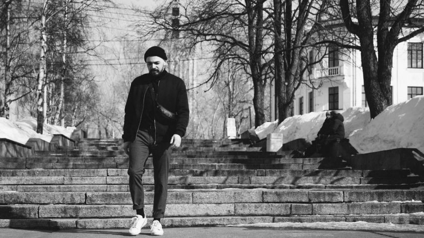A stylish man descends stone stairs in a winter urban scene. Monochrome photography captures the moment.